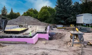 Budowa w stanie zerowym: fundamenty z różową izolacją, zbrojenie, sterta piasku i sprzęt budowlany.