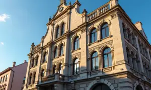 Elegancki budynek z ryzalitem, ozdobiony łukowymi oknami i balkonem, lśni w słońcu.