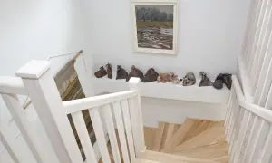 Jasna klatka schodowa z drewnianymi stopniami i balustradą, na półce nad nią rzeźby i obraz.