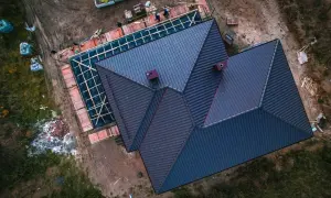 Trwa wymiana dachu na domu jednorodzinnym. Nowe pokrycie z ciemnej dachówki, widoczne kominy i rusztowania.