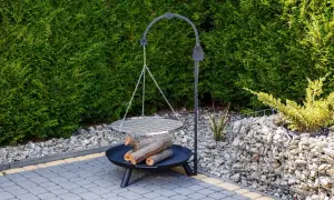 Gotowy grill z polanami drewna, idealny do nauki, jak zrobić grilla. Otoczony zielenią i kamieniami.