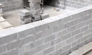 Ściana z bloczków fundamentowych w trakcie budowy. Widoczne stosy pustaków, gotowe do użycia.