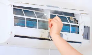 Ręka rozpyla środek do czyszczenia na żeberka klimatyzatora, pokazując, jak odgrzybić klimatyzację w domu.