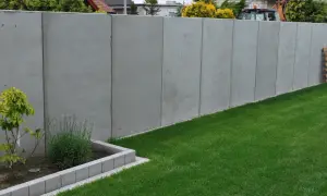 Nowy, betonowy płot w granicy działki. Czy można postawić płot w granicy bez zgody sąsiada? Trawa i rabata kwiatowa.