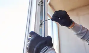 Ręce w rękawiczkach dokonują regulacji drzwi balkonowych uchylnych, dokręcając śrubę kluczem.