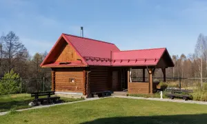 Drewniany domek letniskowy z czerwoną dachem, idealny na wypoczynek. Marzysz o takim? Sprawdź, jak uzyskać dofinansowanie na domek letniskowy.