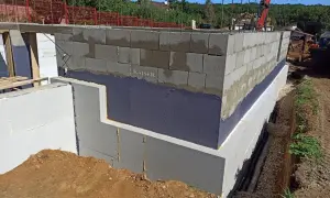 Izolacja fundamentów w starym domu w trakcie prac. Ściany z bloczków betonowych, izolacja przeciwwilgociowa i termiczna.