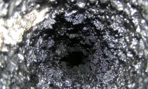 Wnętrze komina pokryte grubą warstwą sadzy i kreozotu, przypominające ciemną, chropowatą jaskinię.