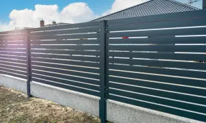 Nowoczesne ogrodzenie z poziomych paneli, co zamiast podmurówki pod ogrodzenie? Betonowy cokół z kamyczkami stanowi estetyczne i trwałe rozwiązanie.