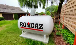 Biały zbiornik na gaz ziemny z napisem ROMGAZ, podłączony do instalacji ogrzewania gazowego z butli.