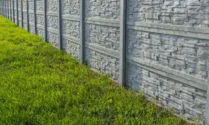 Nowy, betonowy płot z fakturą kamienia, otoczony soczystą zieloną trawą. Idealny do malowania i zabezpieczenia.