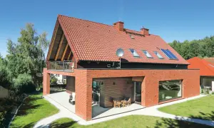 Nowoczesny dom z dachem dwuspadowym 100m2, ceglaną elewacją i dużymi oknami. W ogrodzie ścieżki i zieleń.