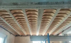 Widok od dołu na budowę, gdzie widoczne są różne rodzaje stropów: betonowe belki i płyty, a także pustaki ceramiczne tworzące łuki.