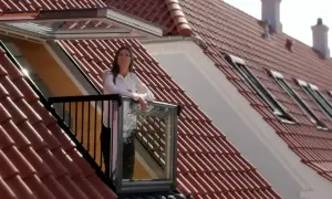 Kobieta na balkonie wychodzącym z okienka w dachu, podziwia widok.