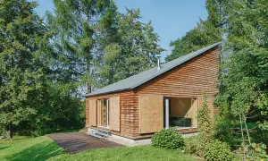 Nowoczesny dom letniskowy z drewnianą elewacją i dużymi przeszkleniami, otoczony zielenią.