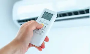 Dłoń trzymająca pilot do klimatyzacji, ustawiająca ogrzewanie. Na ekranie widoczna temperatura 26°C.