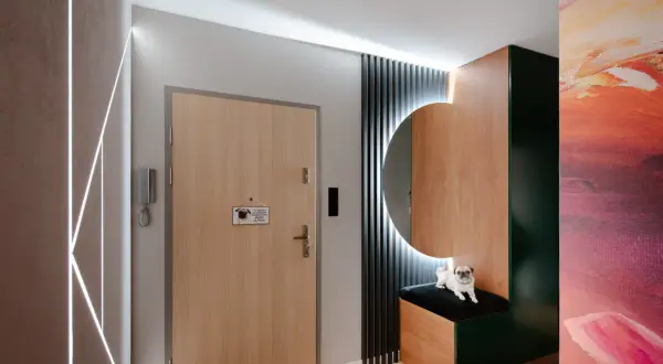 Nowoczesny przedpokój z drewnianymi elementami, lustrem i pieskiem rasy mops.