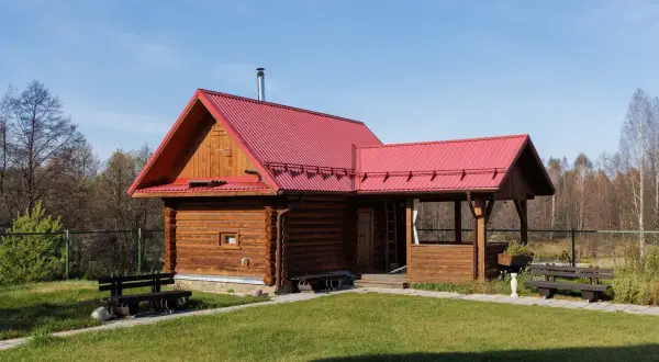 Drewniany domek letniskowy z czerwoną dachem, idealny na wypoczynek. Marzysz o takim? Sprawdź, jak uzyskać dofinansowanie na domek letniskowy.