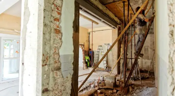 Remont wnętrza, gdzie pracownik na drabinie wzmacnia strop nad otworem w ścianie nośnej.
