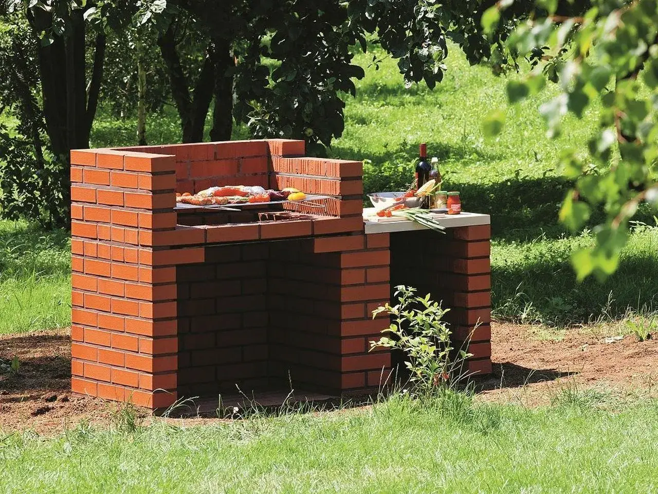Prosty murowany grill z cegły, gotowy do przyjęcia gości. Na ruszcie już leżą smakołyki, a obok butelka wina i warzywa.