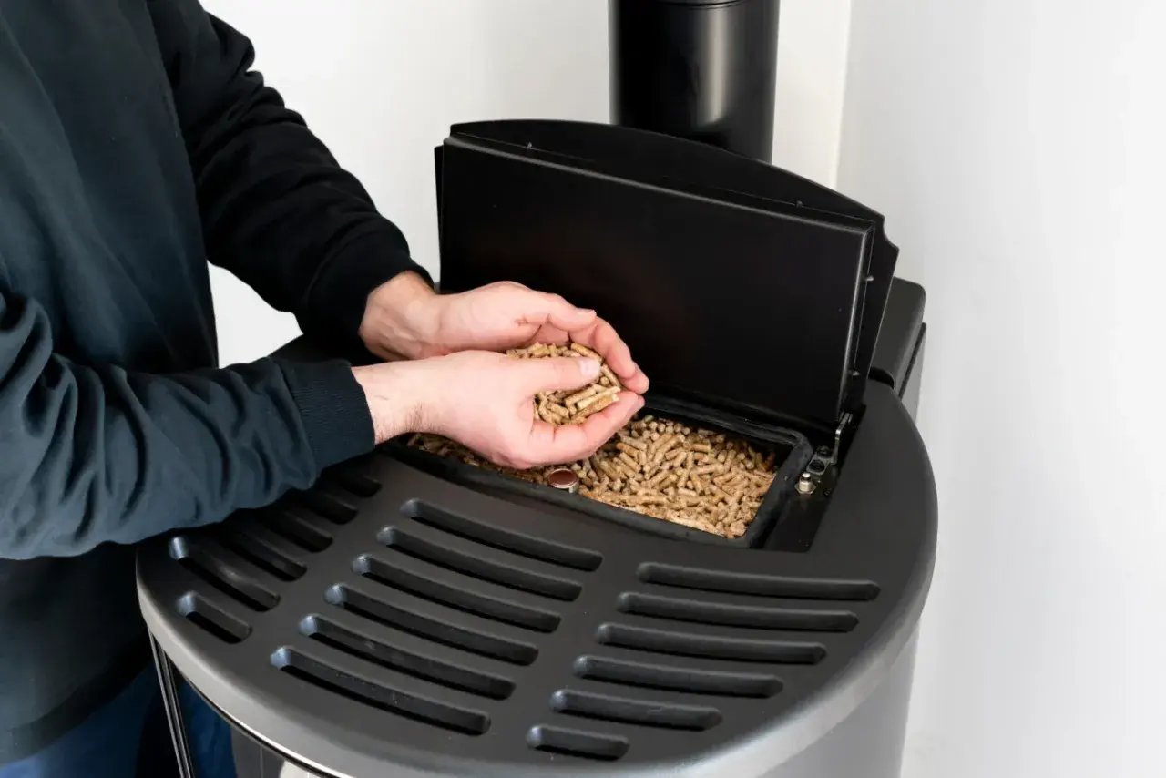 Mężczyzna wsypuje pellet do nowoczesnego pieca. Dofinansowanie do pieca na pellet to świetny sposób na ekologiczne ogrzewanie.