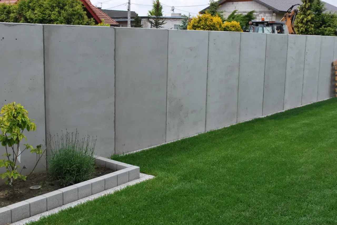 Nowy, betonowy płot w granicy działki. Czy można postawić płot w granicy bez zgody sąsiada? Trawa i rabata kwiatowa.