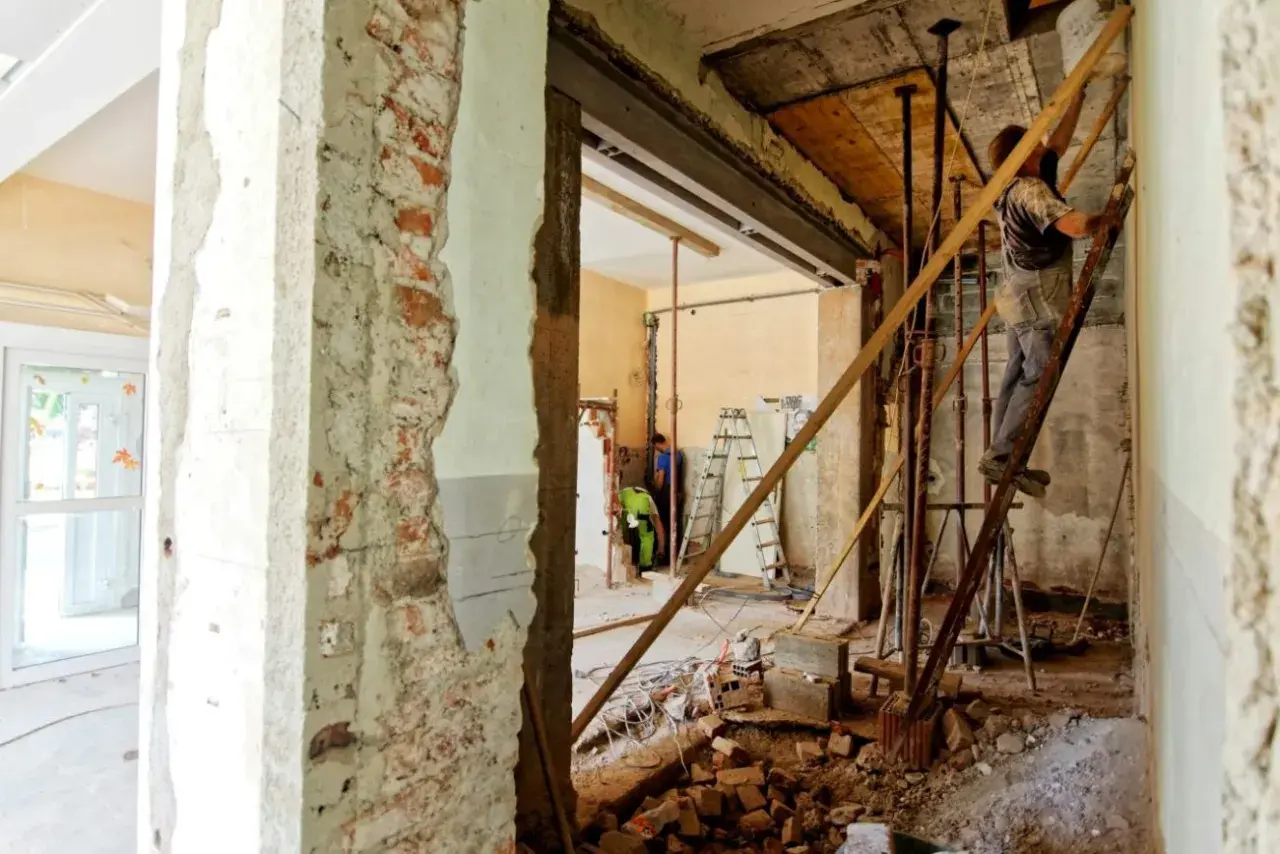 Remont wnętrza, gdzie pracownik na drabinie wzmacnia strop nad otworem w ścianie nośnej.