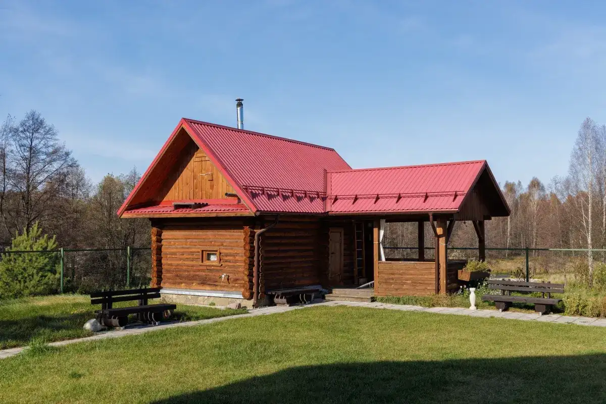 Drewniany domek letniskowy z czerwoną dachem, idealny na wypoczynek. Marzysz o takim? Sprawdź, jak uzyskać dofinansowanie na domek letniskowy.