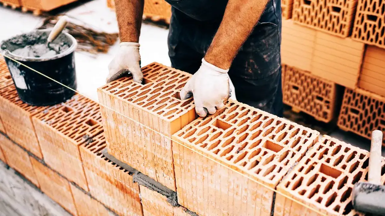 Budowa domu 100m2 wymaga precyzji. Murarz układa pustaki ceramiczne, przygotowując się do obliczenia, ile cegły na dom 100m2 będzie potrzebne.