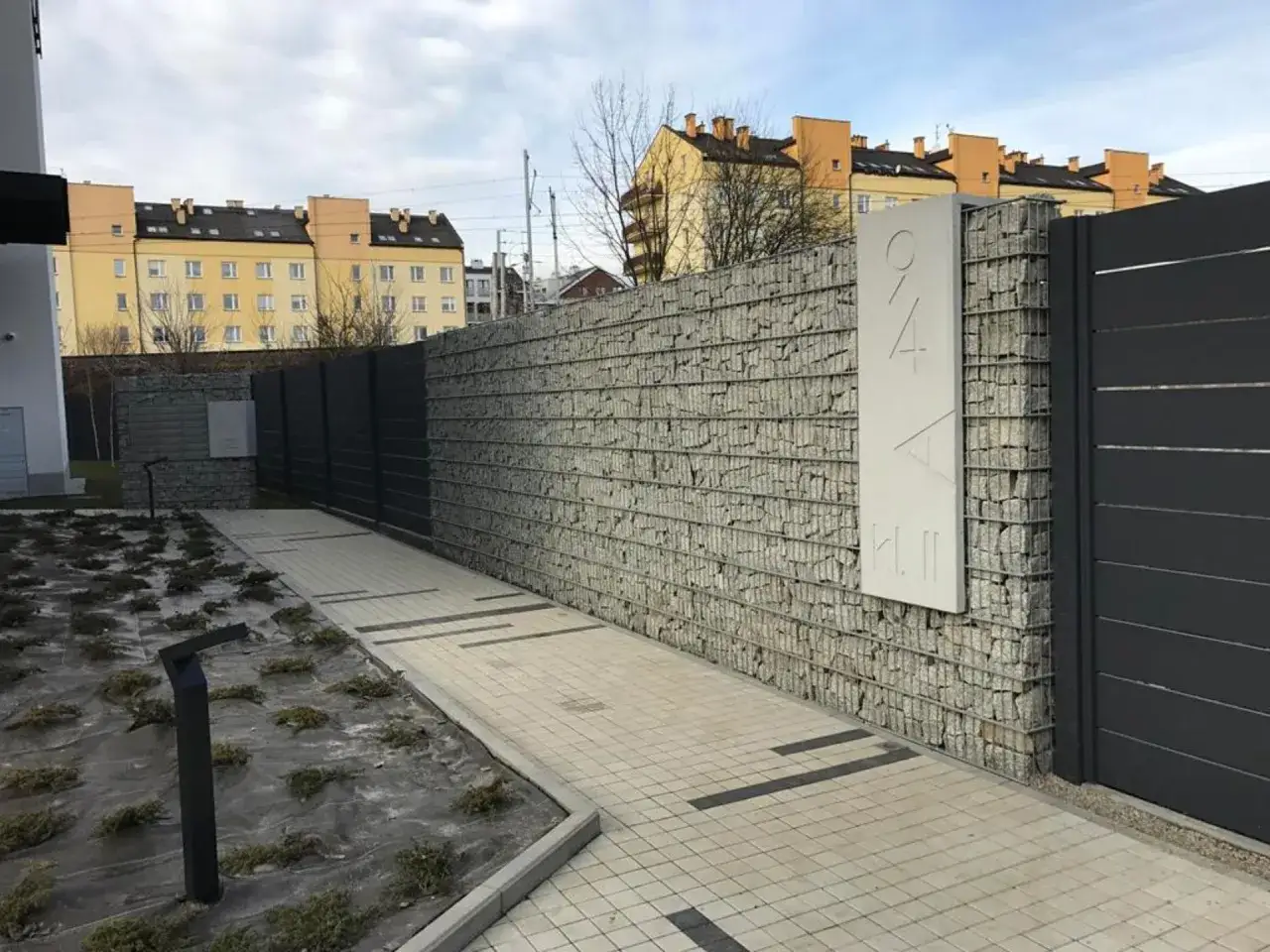Nowoczesny pomysł na ogrodzenie domu: gabionowa ściana z kamienia i ciemny panel. Elegancko i praktycznie.