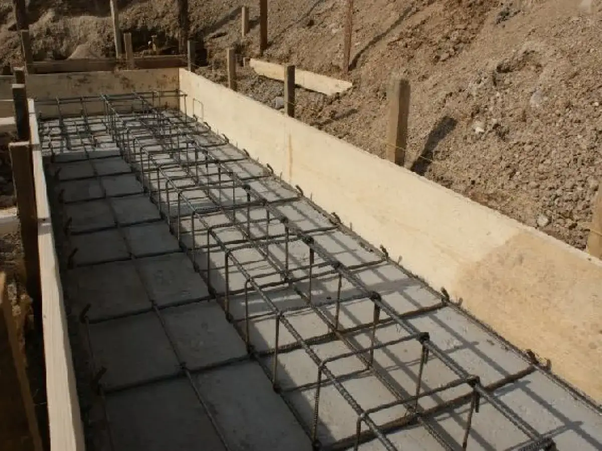 Zbrojenie fundamentów w drewnianej szalunkach. Widać siatkę stalowych prętów, gotową do zalania betonem. To kluczowy etap, by wiedzieć, ile bloczków na fundament będzie potrzebnych.
