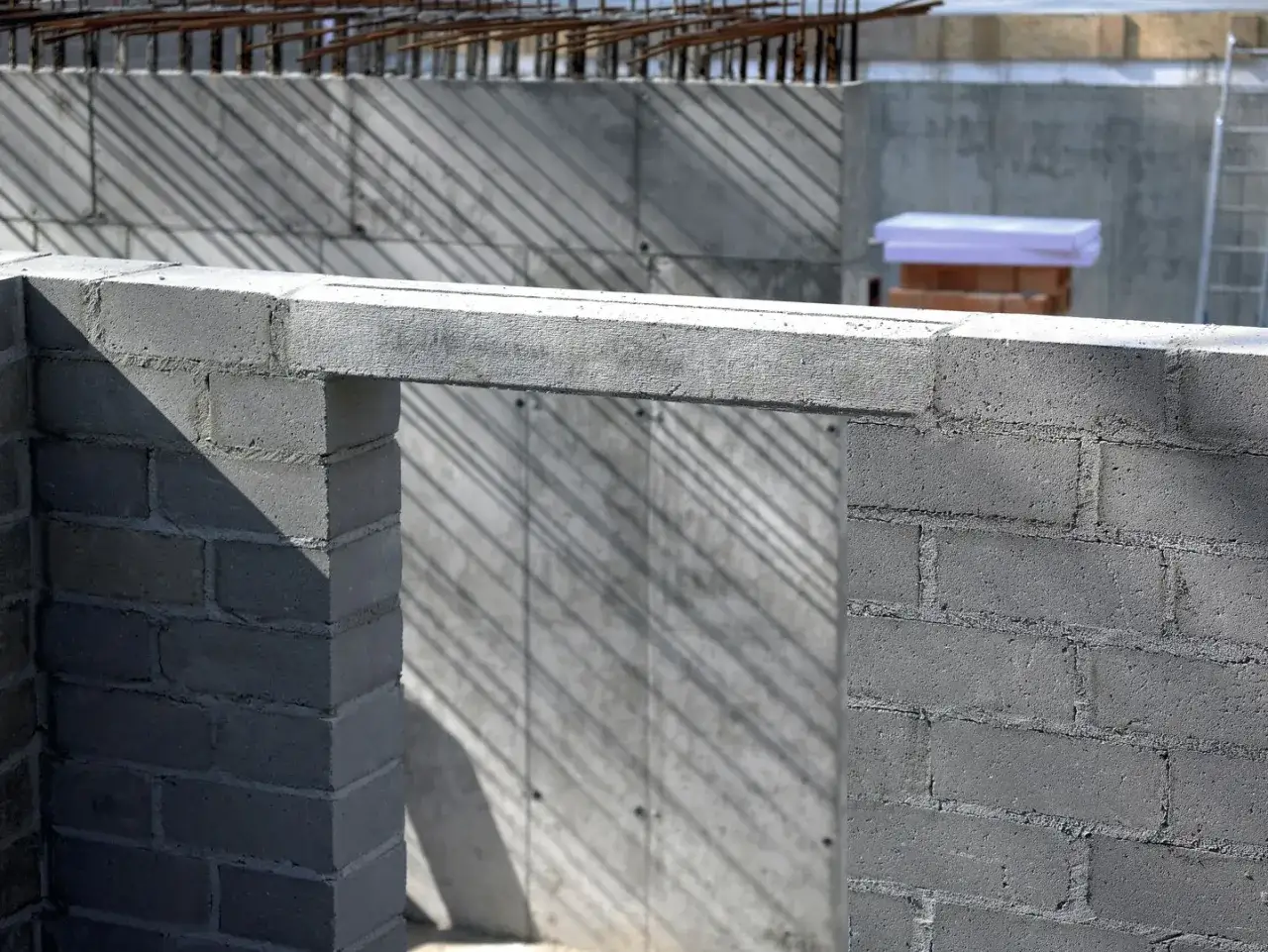 Betonowe nadproże nad otworem w budowie, z widocznymi cieniami na tle betonowej ściany.