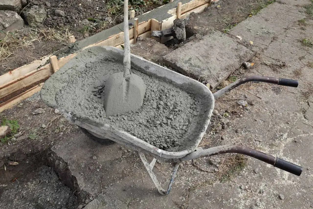 Taczka z betonem i łopatą czeka na wylanie ław fundamentowych.