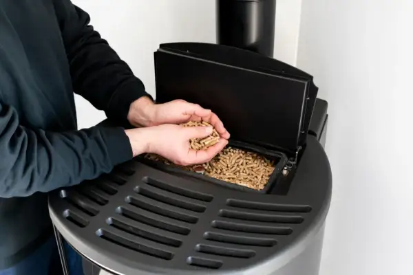 Mężczyzna wsypuje pellet do nowoczesnego pieca. Dofinansowanie do pieca na pellet to świetny sposób na ekologiczne ogrzewanie.