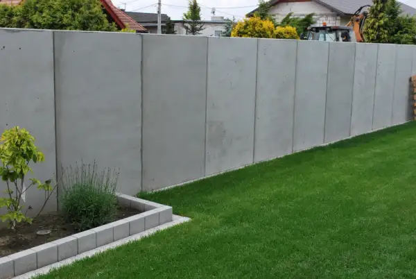Nowy, betonowy płot w granicy działki. Czy można postawić płot w granicy bez zgody sąsiada? Trawa i rabata kwiatowa.