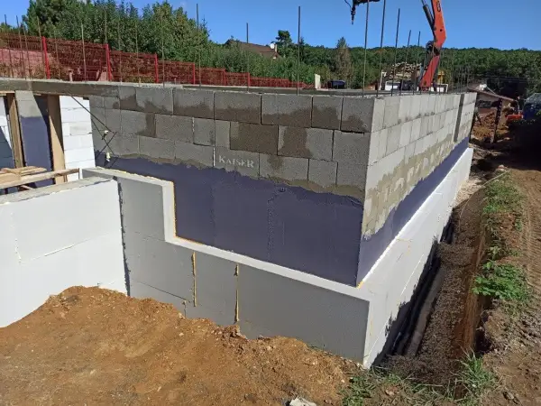 Izolacja fundamentów w starym domu w trakcie prac. Ściany z bloczków betonowych, izolacja przeciwwilgociowa i termiczna.