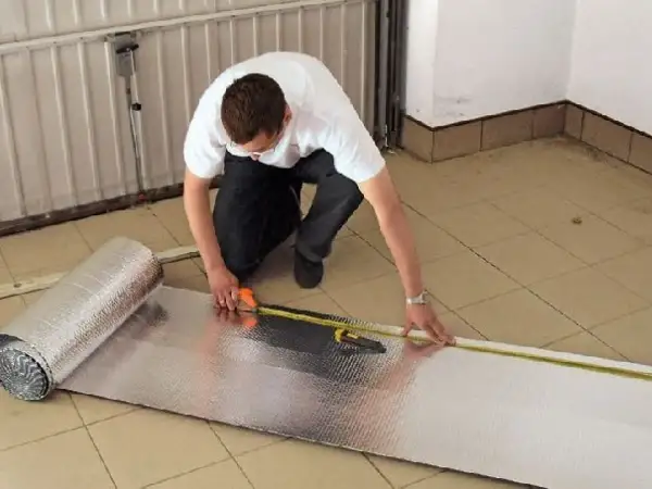 Mężczyzna mierzy materiał do ocieplenia bramy garażowej.