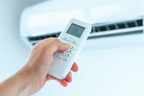 Dłoń trzymająca pilot do klimatyzacji, ustawiająca ogrzewanie. Na ekranie widoczna temperatura 26°C.