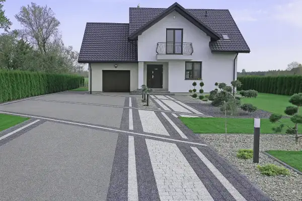 Nowoczesny podjazd do domu z geometrycznymi wzorami z kostki brukowej, prowadzący do białego domu z garażem i zadbanym ogrodem.