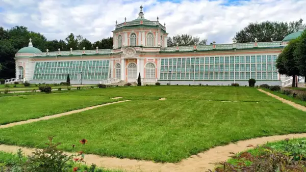 Przepiękny, różowo-zielony pałac z przeszklonymi ścianami, przypominający **ogród zimowy w domu**, otoczony jest zadbanym trawnikiem i alejkami.