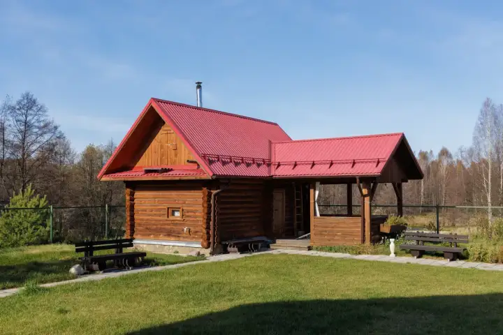 Drewniany domek letniskowy z czerwoną dachem, idealny na wypoczynek. Marzysz o takim? Sprawdź, jak uzyskać dofinansowanie na domek letniskowy.
